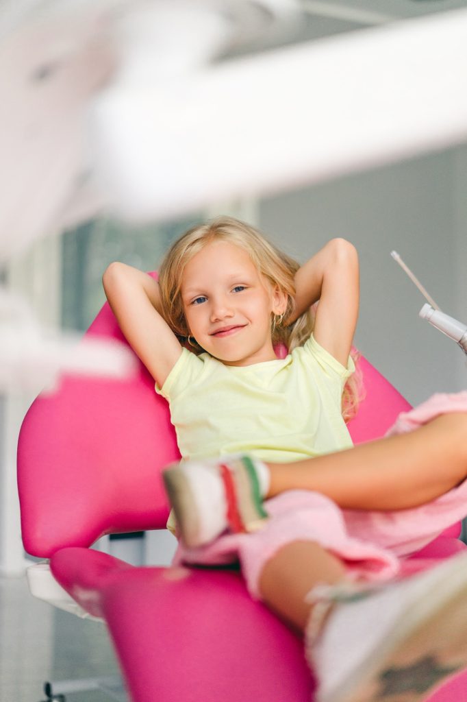 smiling kid looking at camera awhile sitting in chair at dentist office